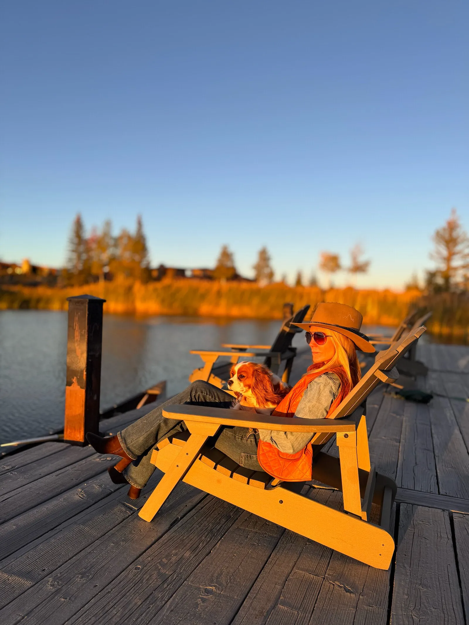Natalie relaxing in an Adirondack chair on a lake dock at golden hour, with George, her Cavalier King Charles spaniel, in her lap